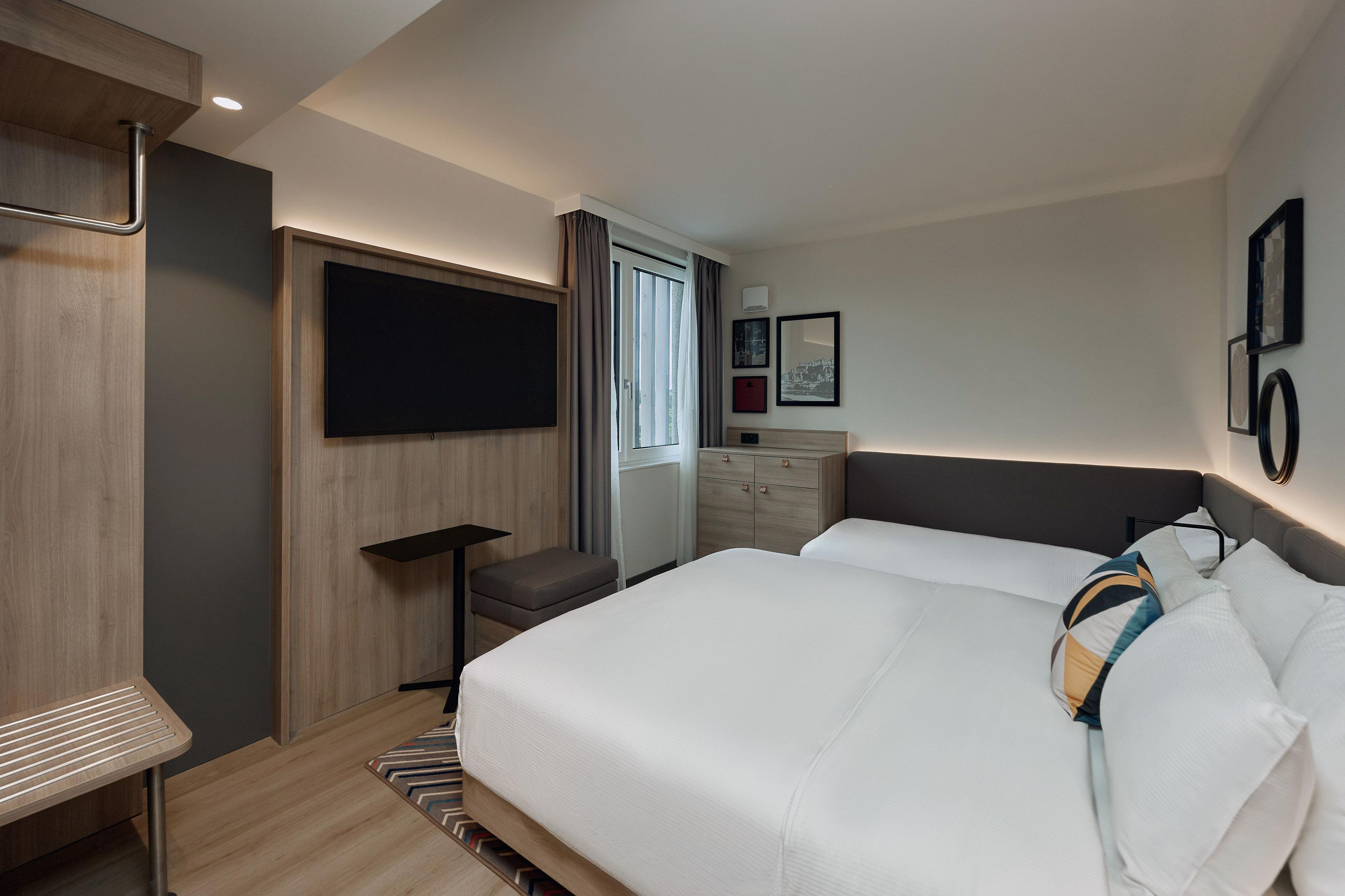 A hotel room with a bed, a TV, a dresser, and a window.
