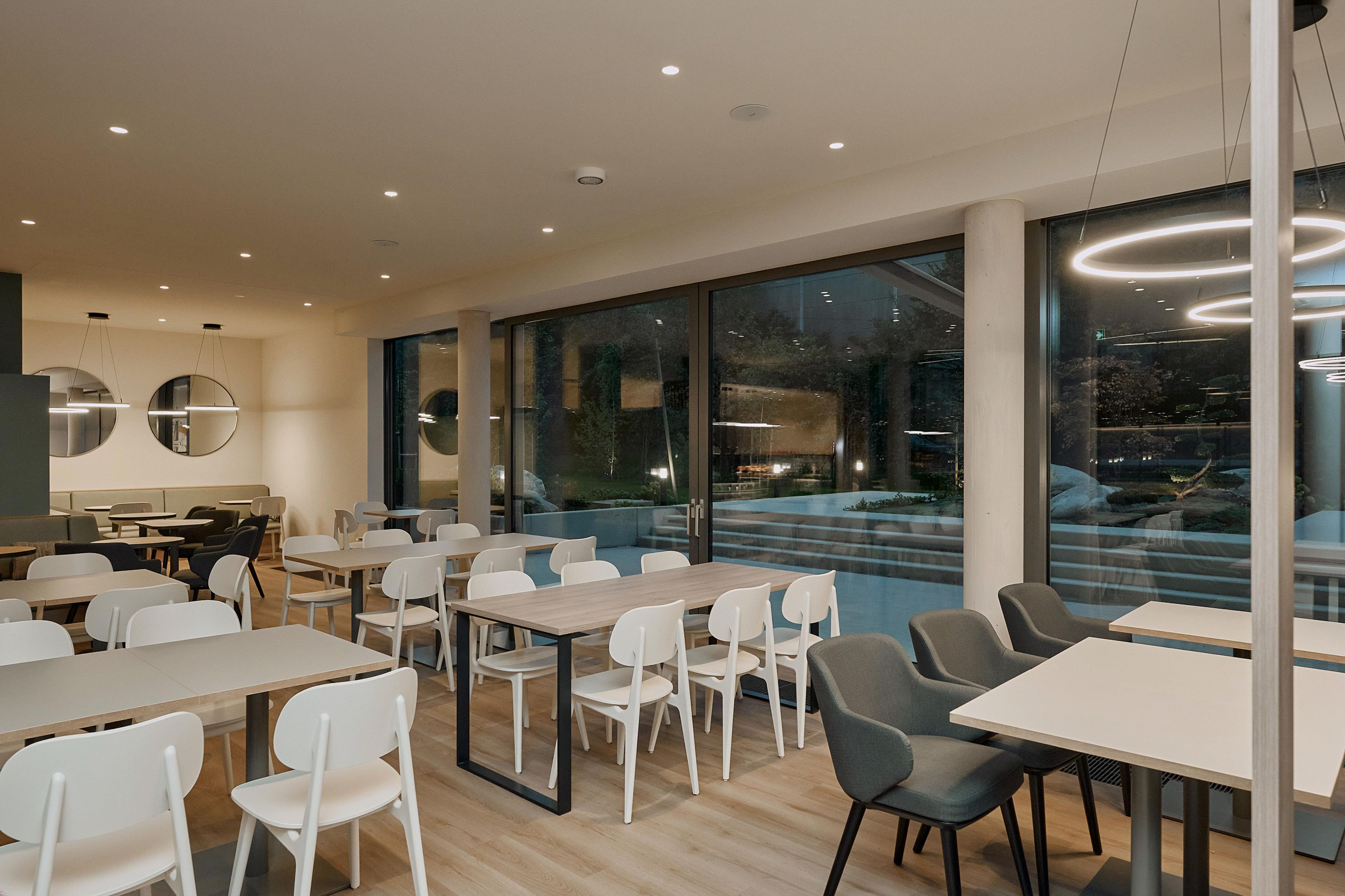 A modern dining area with tables and chairs, large windows, and a view of the outdoors.