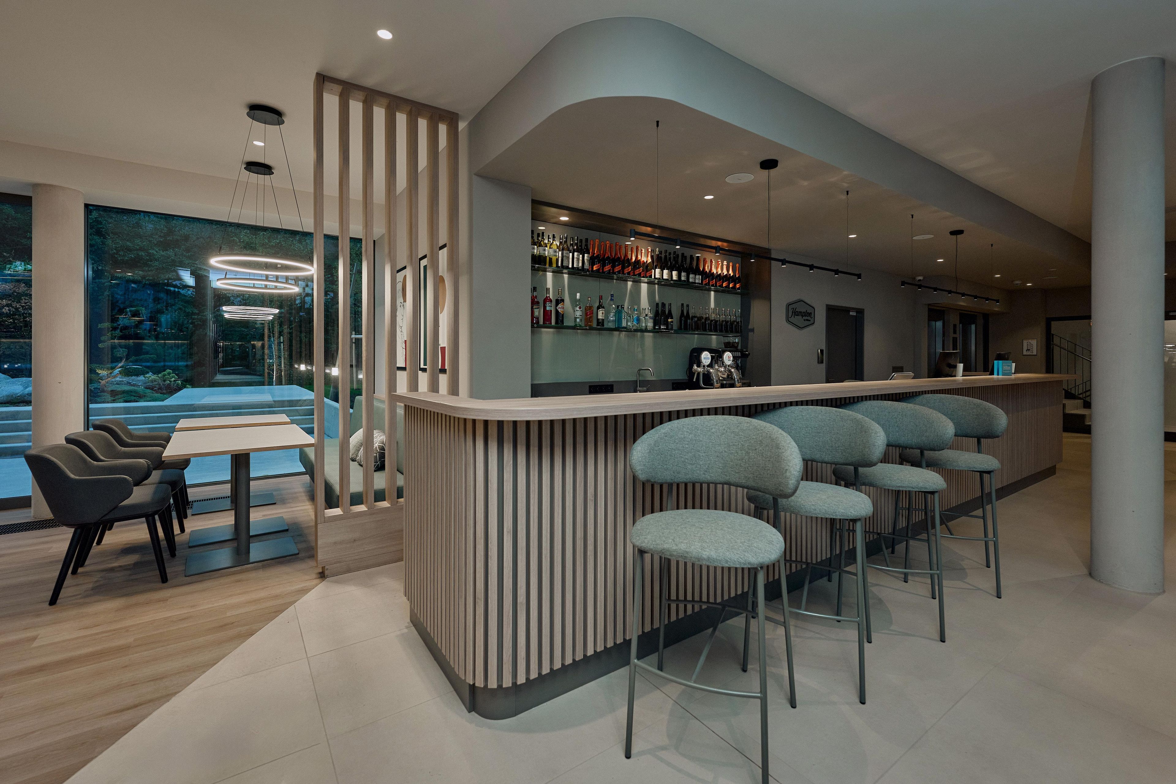 Un área de bar moderna con una barra curva, taburetes y una vitrina con bebidas.