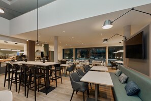 Un comedor moderno con mesas y sillas, una barra con un menú, y un ventanal con vistas.