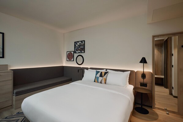 Une chambre d’hôtel moderne équipée d’un grand lit, d’une table de chevet, d’un bureau et d’une armoire.