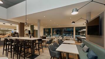 A modern dining area with tables and chairs, a counter with a menu, and a large window offering a view.