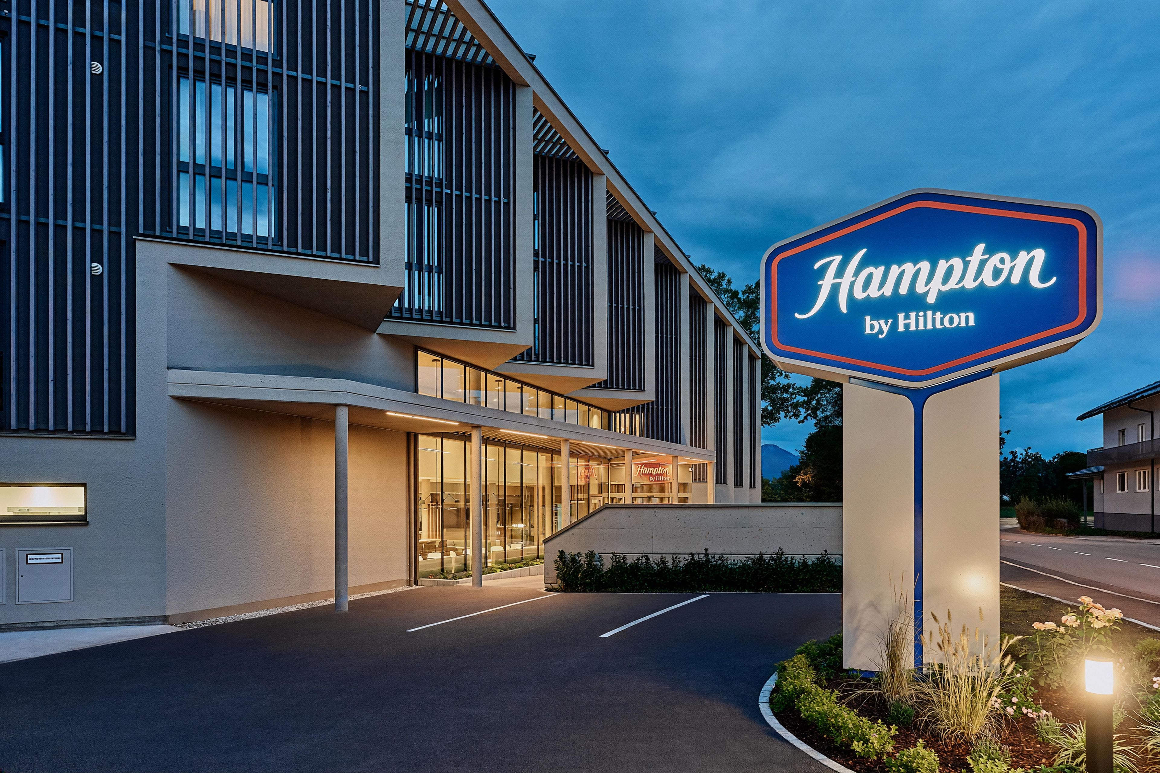 A modern hotel building with a prominent sign for Hampton by Hilton.