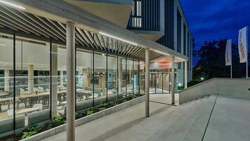 Un edificio moderno con un área de estar al aire libre techada, ventanas amplias y un letrero que dice 'Hampton by Hilton'.
