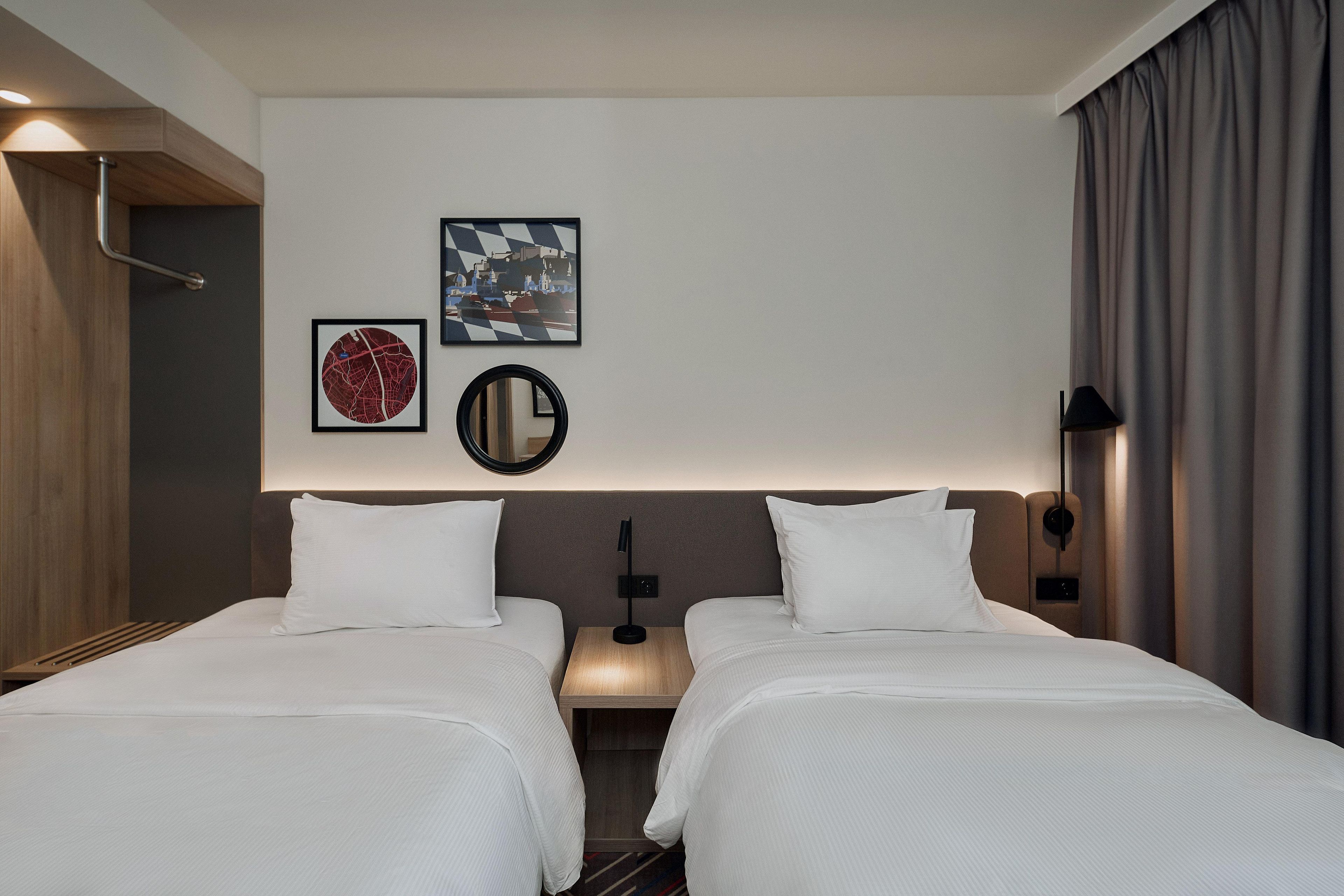 Une chambre d’hôtel avec deux lits, une table de chevet avec une lampe et des œuvres d’art accrochées au mur.