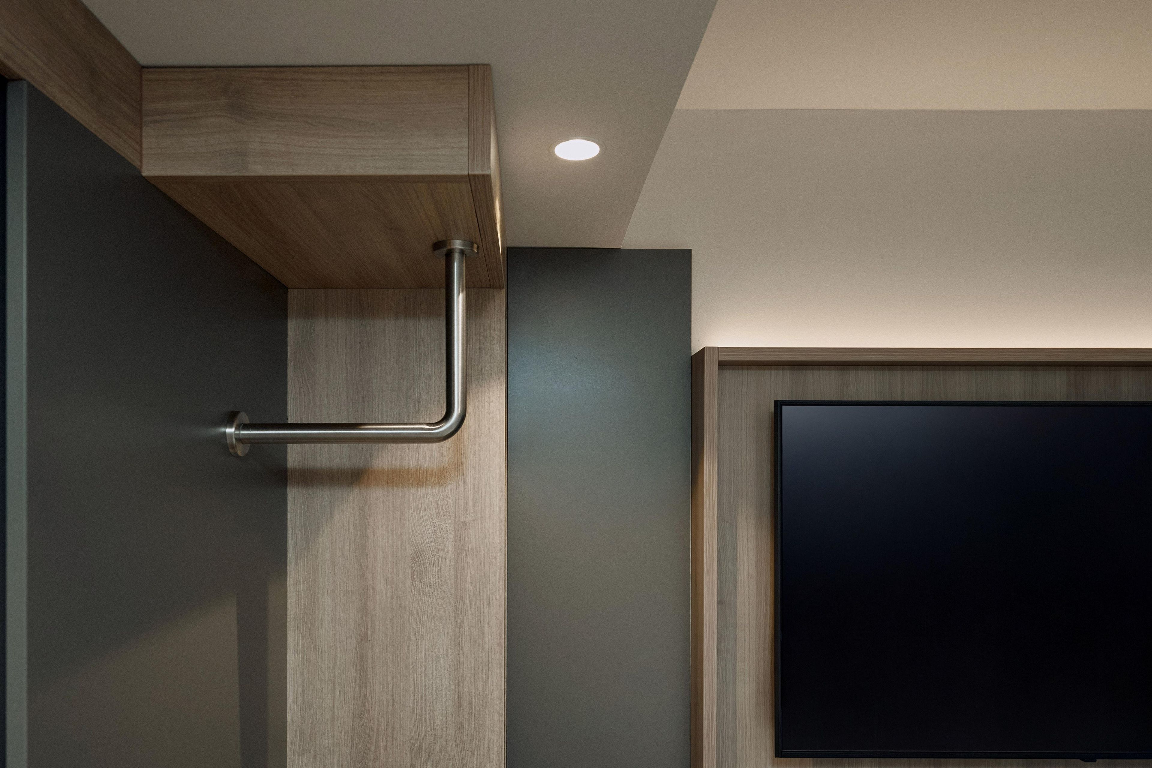 A modern bathroom with a wooden vanity, a towel rack, and a flat-screen TV mounted on the wall.