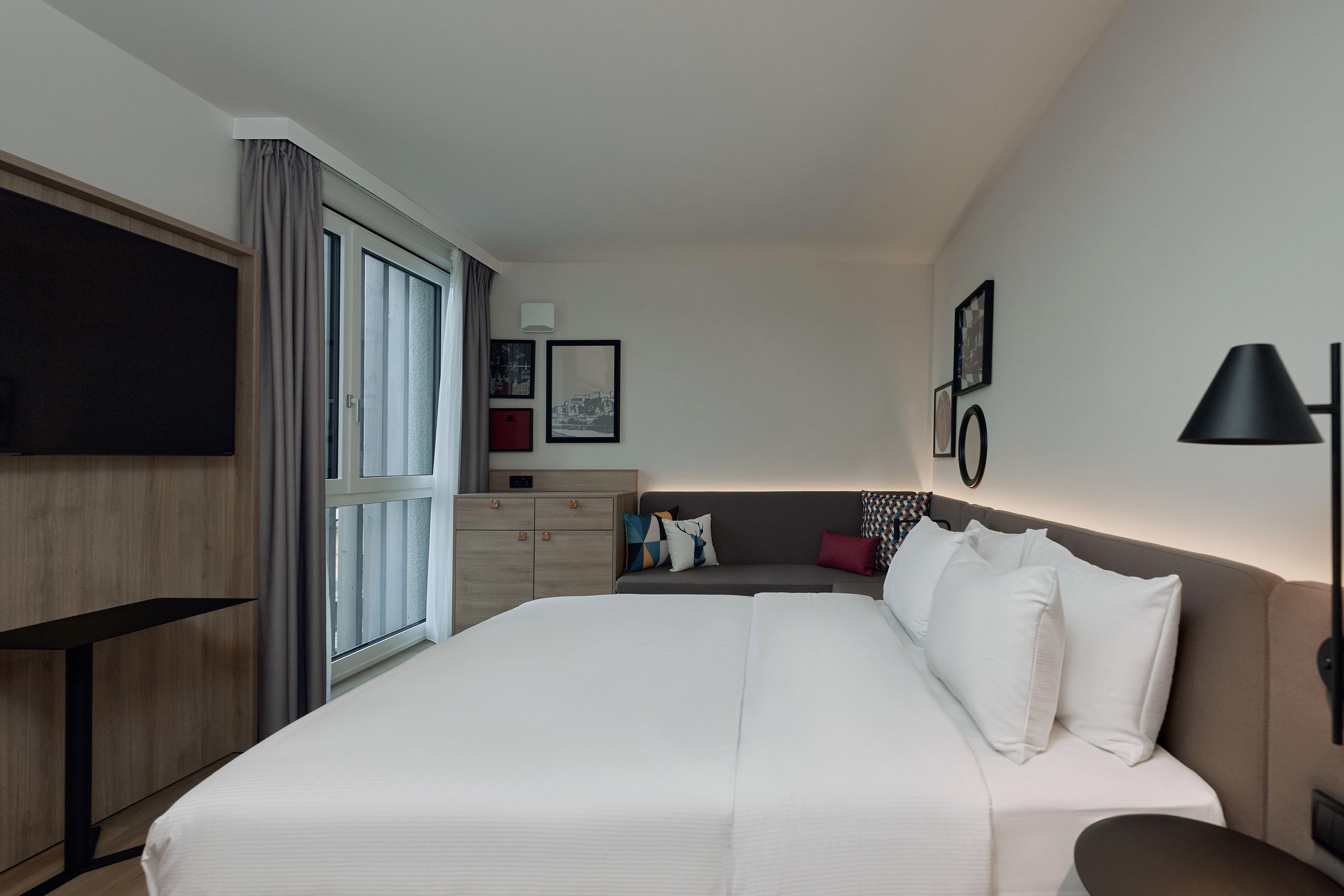 A hotel room with a large bed, a desk, a wardrobe, and a TV.