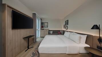 Ein Hotelzimmer mit einem großen Bett, einem an der Wand montierten Fernseher, einem Schreibtisch, einem Sessel und einem Nachttisch.