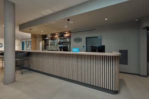 A modern bar area with a wooden counter, a digital screen, and a selection of bottles. - Hampton By Hilton Salzburg Messe (Salzburg)