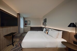Moderni hotellihuone, jossa on suuri sänky, työpöytä, tuoli ja seinälle asennettu televisio.