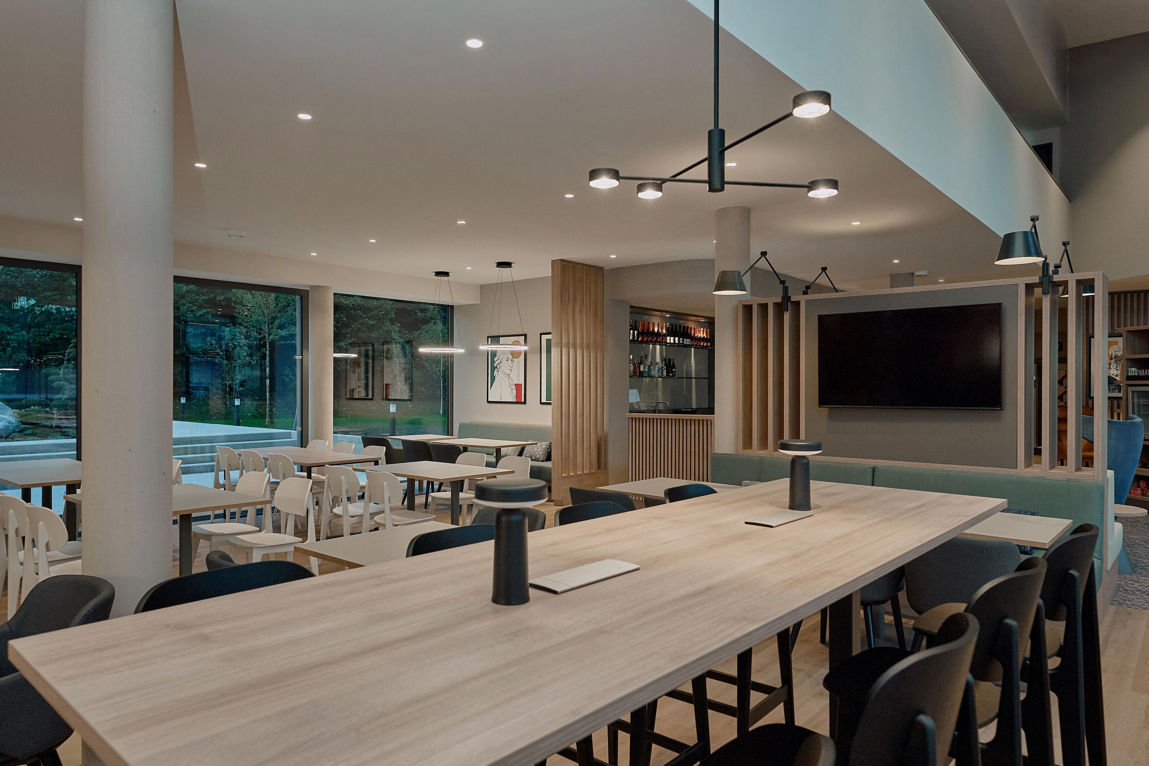 A modern dining area with a long wooden table, multiple chairs, and pendant lighting.