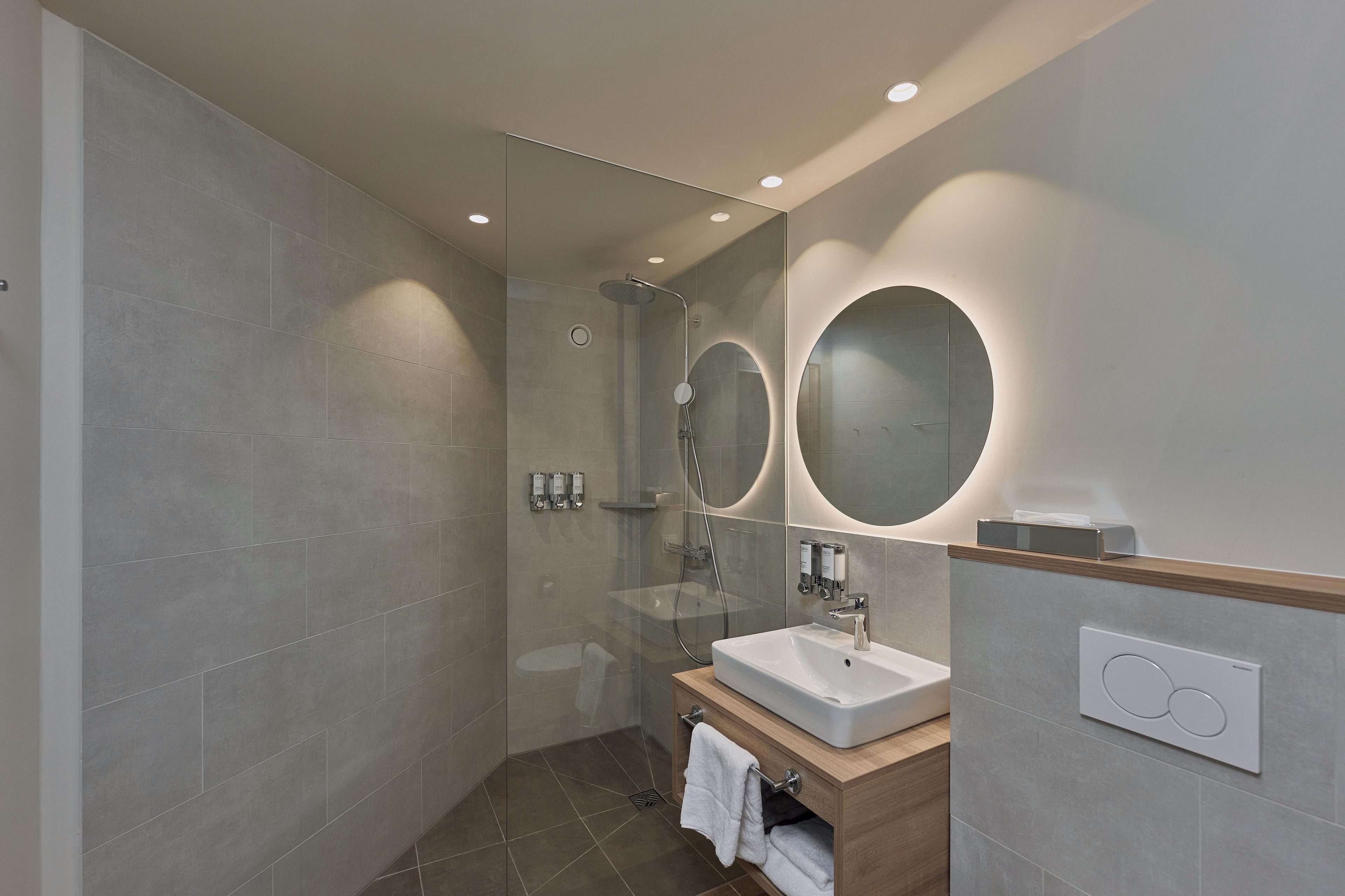Une salle de bain moderne avec une douche à parois de verre, un lavabo avec un meuble-vasque en bois et deux miroirs fixés au mur.