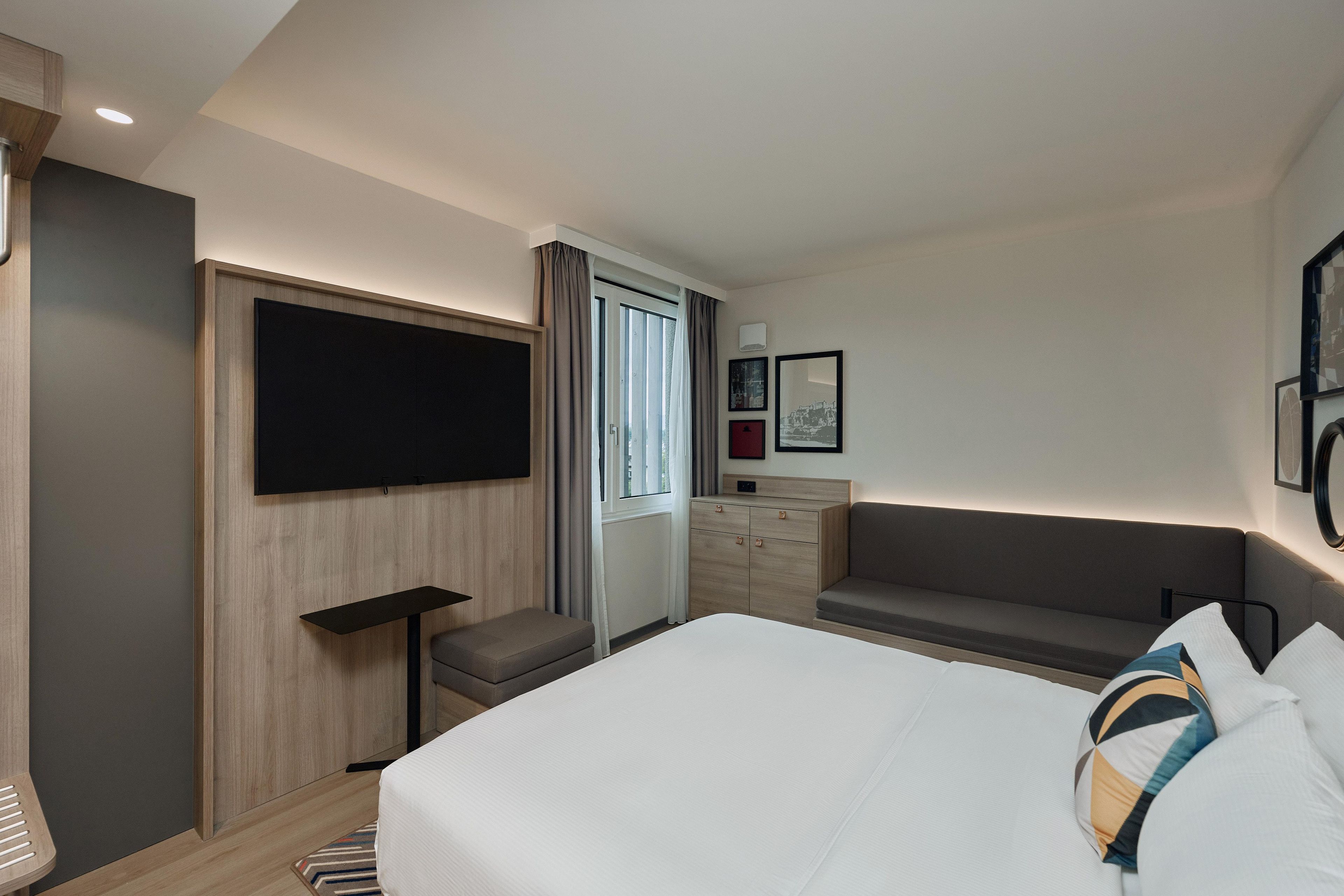 A hotel room with a bed, a seating area, a television, and a window with curtains.