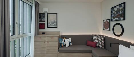 Habitación de hotel moderna con una cama grande, un sofá, un aparador de madera y vistas a la ciudad.
