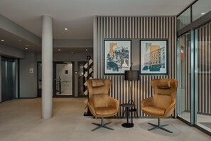Un hall con dos sillones de cuero, una mesita y dos cuadros con vistas urbanas en la pared.