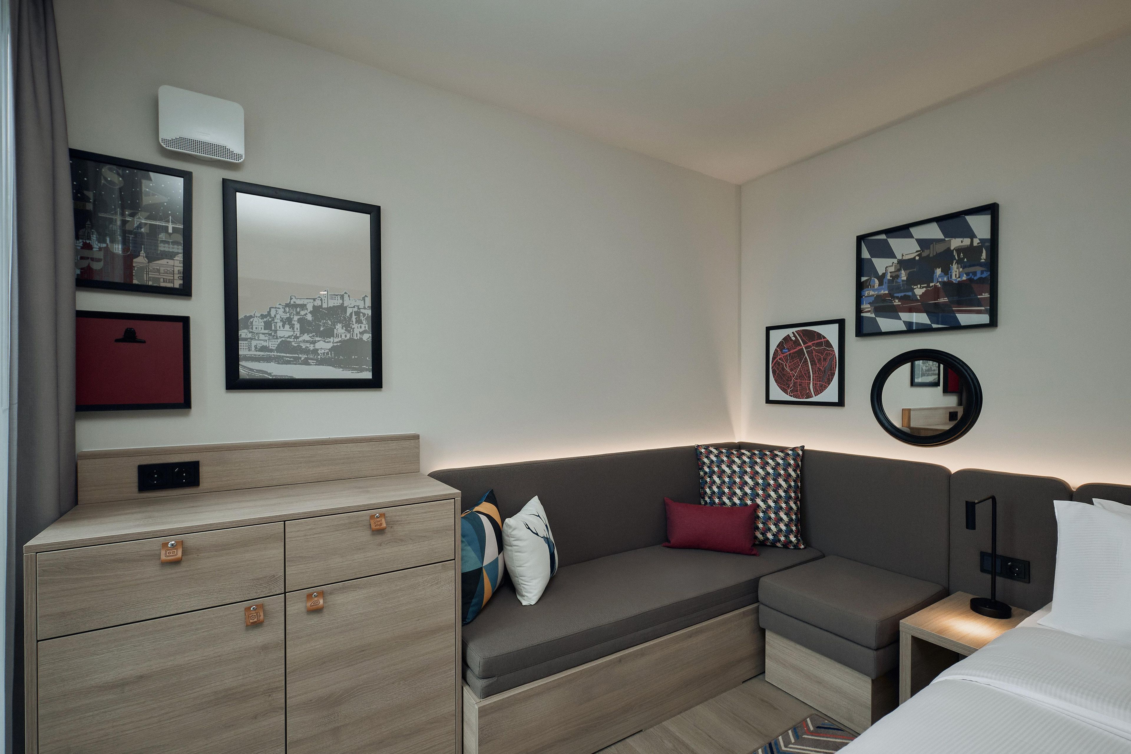 Een moderne hotelkamer met een bank, een klein nachtkastje, een dressoir en kunstwerken aan de muur.