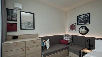 Een moderne hotelkamer met een bank, een klein nachtkastje, een dressoir en kunstwerken aan de muur.