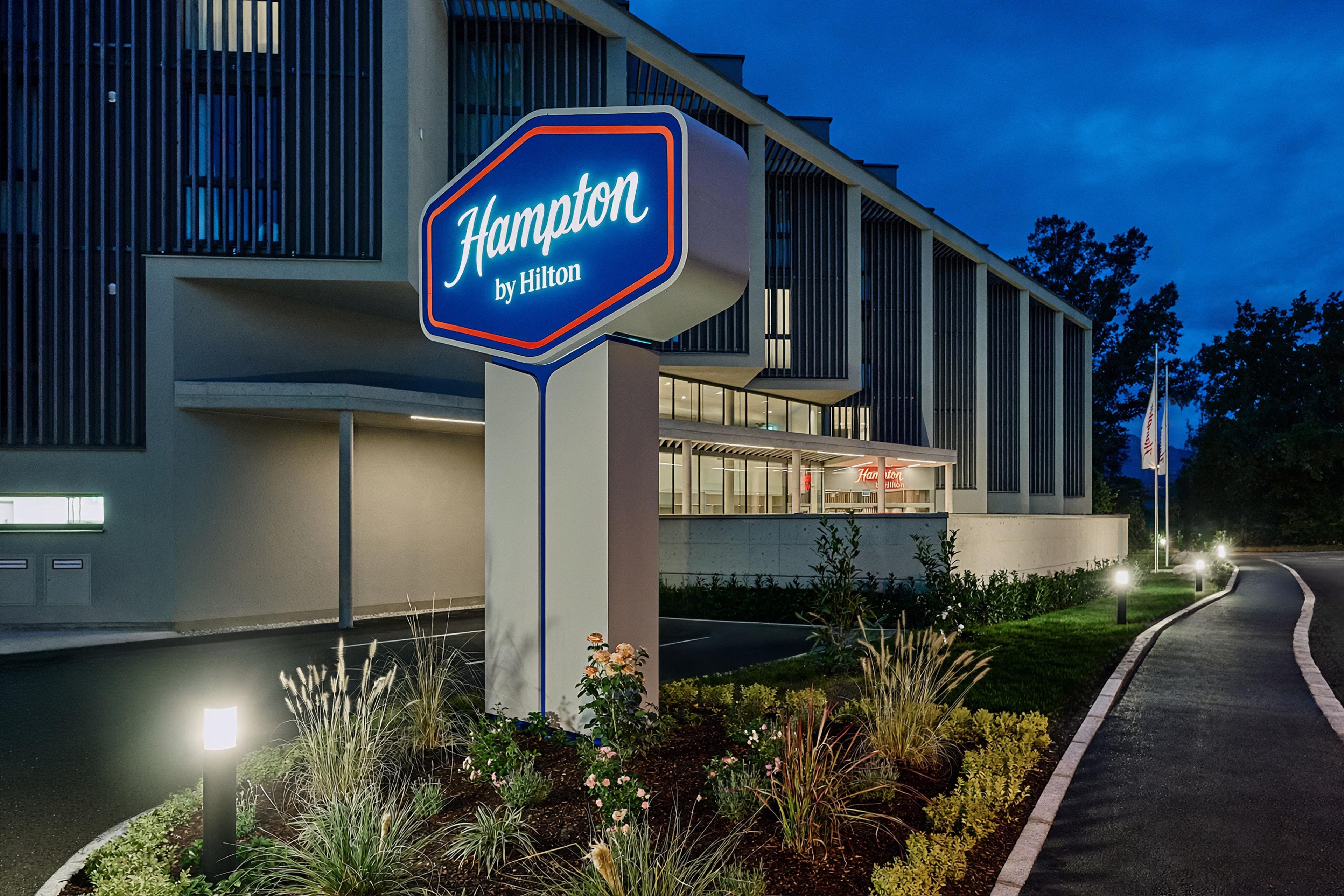 Segnaletica di un hotel con la scritta 'Hilton Hampton' e un edificio moderno caratterizzato da ampie finestre e un tetto piatto.