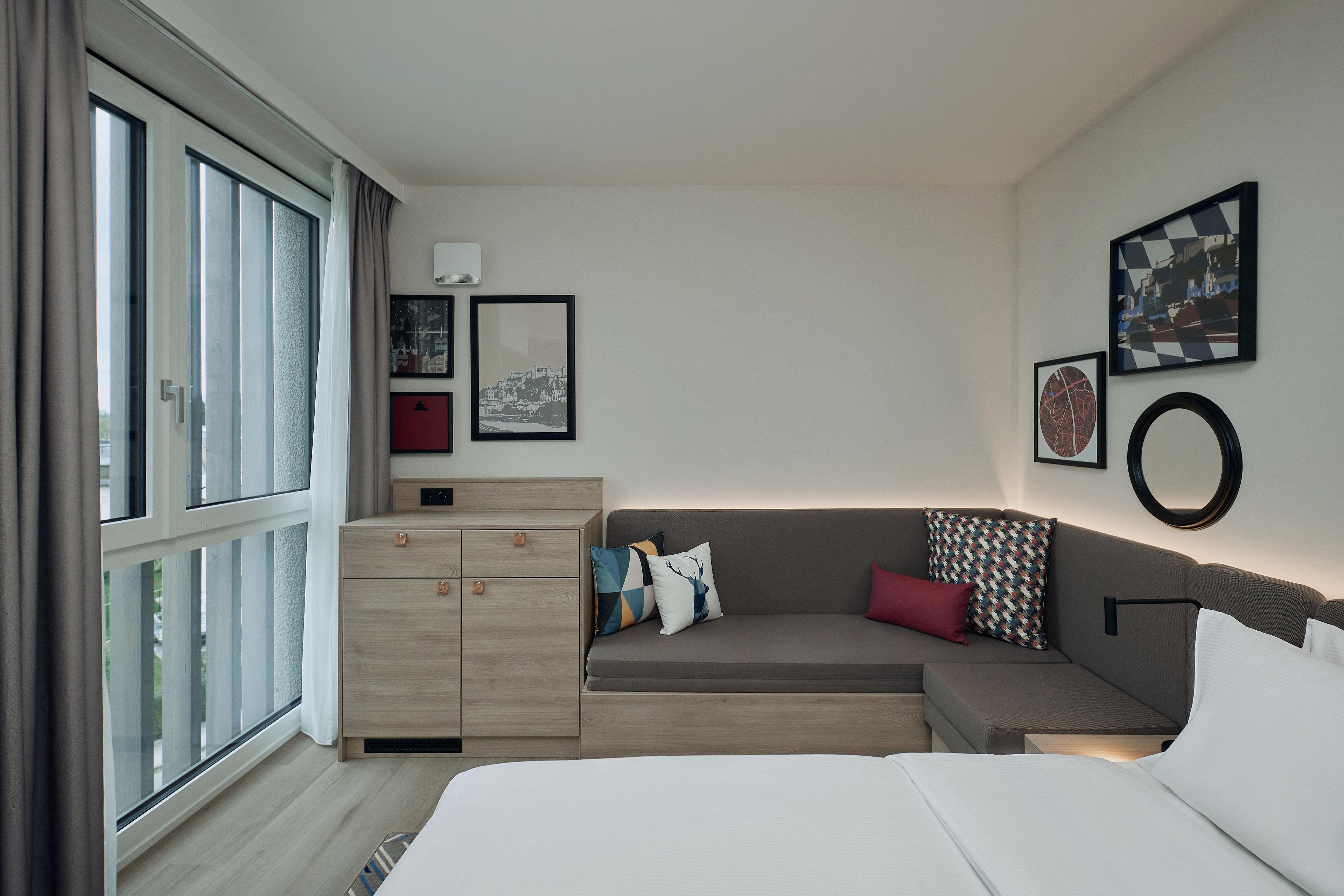 Una camera d'hotel moderna con un letto grande, un divano, un comò in legno e vista sulla città.