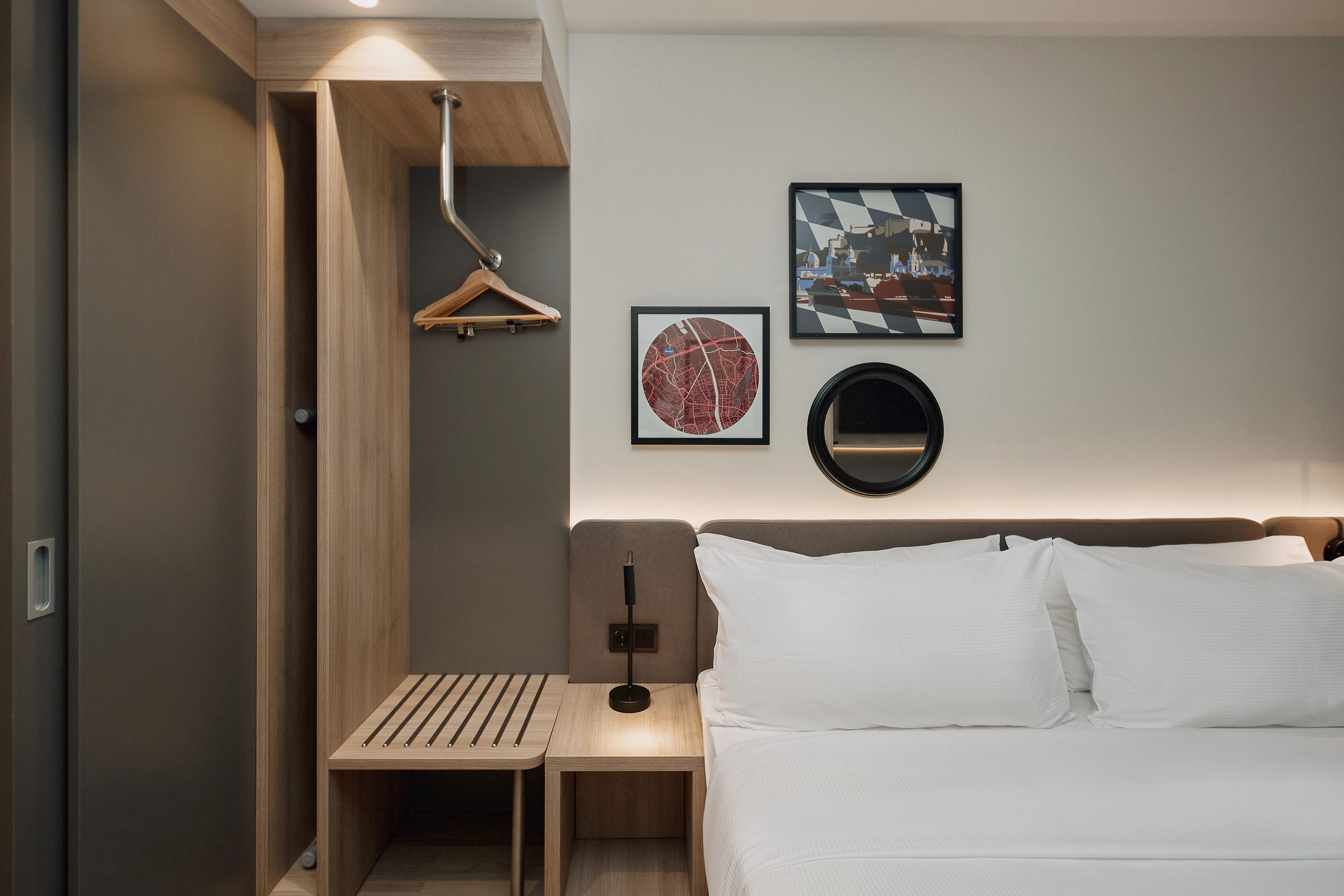 A hotel room with a bed, a bedside table, a hanging light, and two wall-mounted artworks.