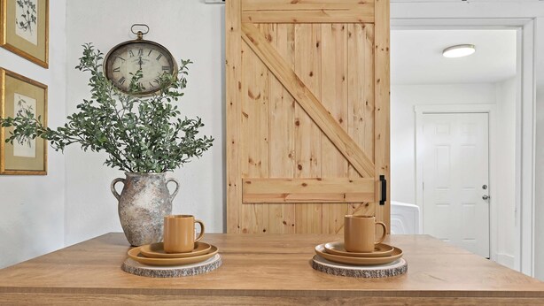 A wooden table with two cups and saucers, a vase with a plant, and a wall clock. - The 408 Family Farmhouse (Siloam Springs)