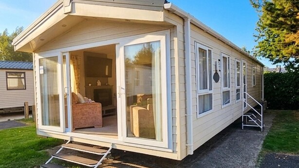A mobile home with a porch, a fireplace, and a set of stairs leading to the entrance. - Modern & Spacious 40ft Caravan Sleeps 6, Luxury! (Great Yarmouth)
