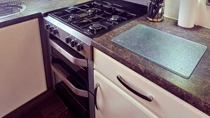 Una cocina con estufa, horno y una encimera con tabla de cortar.