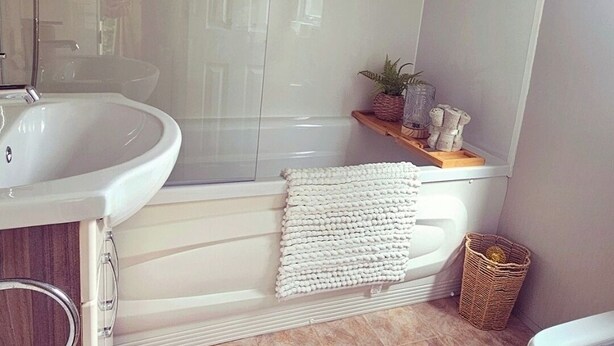 A bathroom with a white bathtub, a sink, and a shower. There is a wicker basket and a small plant on the shelf. - Modern & Spacious 40ft Caravan Sleeps 6, Luxury! (Great Yarmouth)