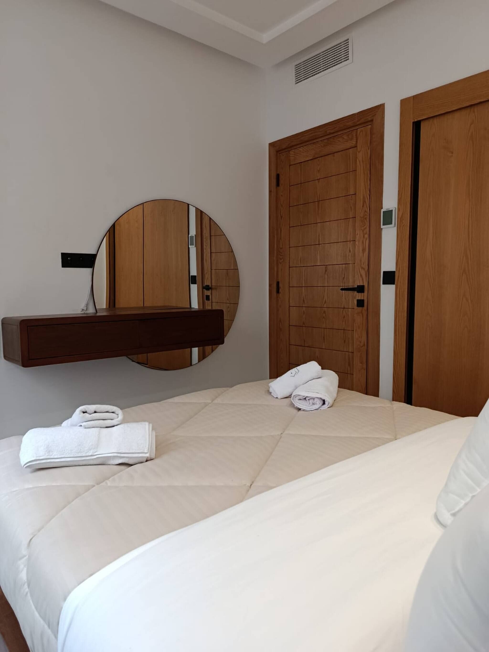 A bedroom with a bed, a round mirror, and two wooden doors.
