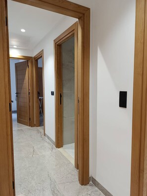 A hallway with wooden doors, a tiled floor, and a light switch on the wall. - Charming 2-bedroom Apartment in Tunis With City Views (La Marsa)