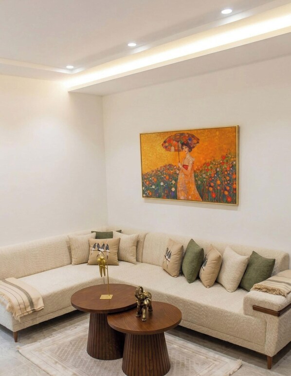 Una sala de estar moderna con un sofá seccional color beige, dos mesas de centro redondas de madera y un cuadro grande en la pared.
