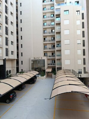 Un área de estacionamiento con marquesinas cubiertas y un edificio con la etiqueta 'BLOC B' al fondo.