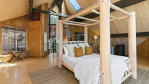 Un lit à baldaquin en bois dans une cabane dotée d’une lucarne, d’une petite table et d’une chaise.
