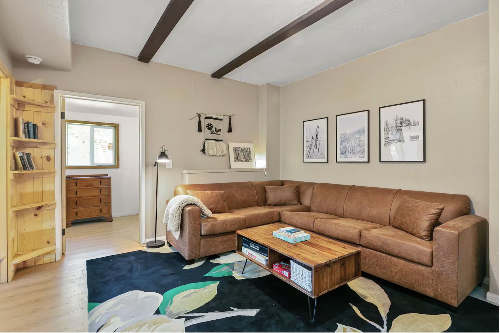 A living room with a sectional sofa, a coffee table, a bookshelf, and framed pictures on the wall.