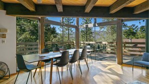 Un espace repas avec une longue table, des chaises et une vue sur les arbres à travers de grandes fenêtres en verre.