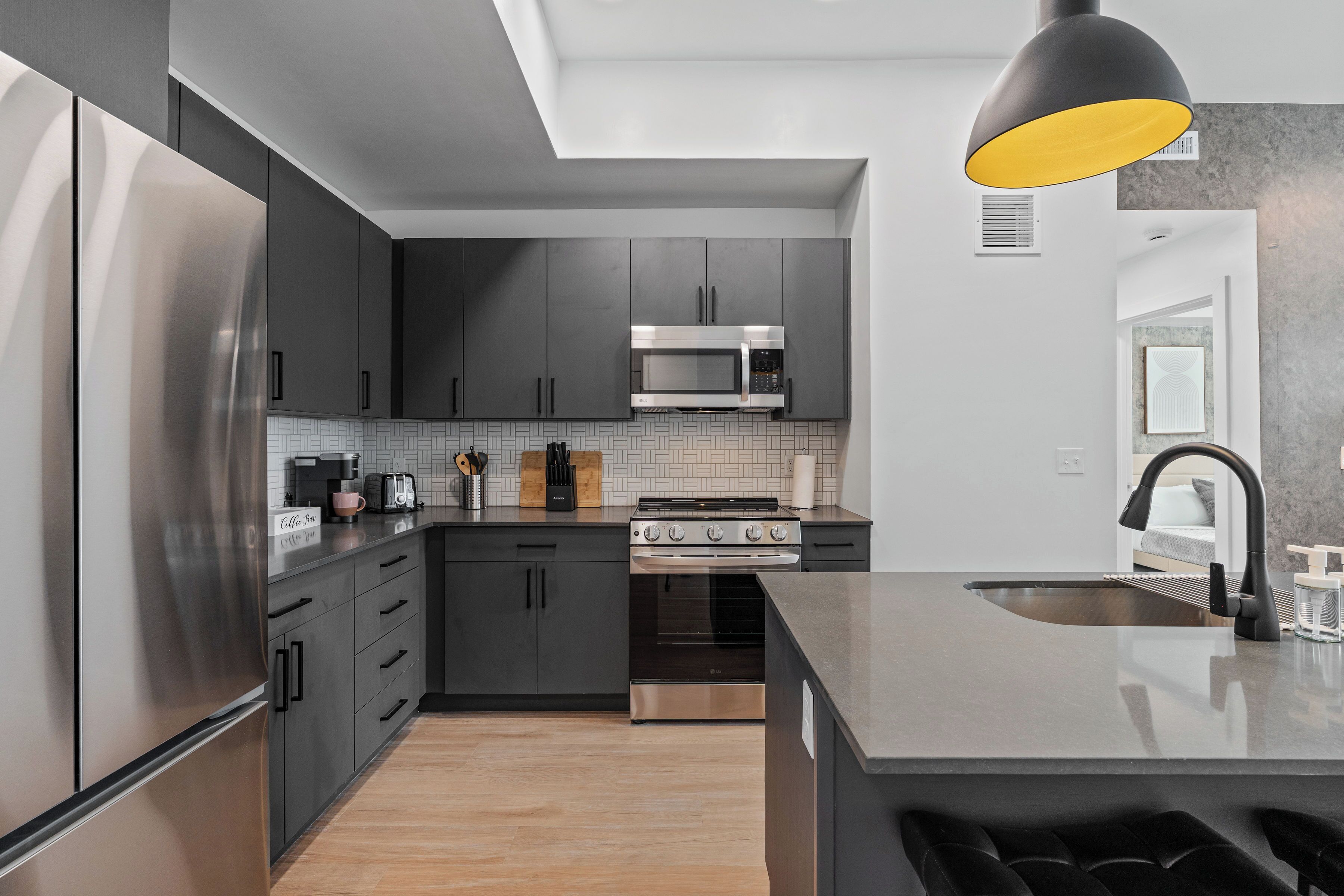 Una cocina moderna con armarios oscuros, electrodomésticos de acero inoxidable, una isla central y una lámpara colgante.