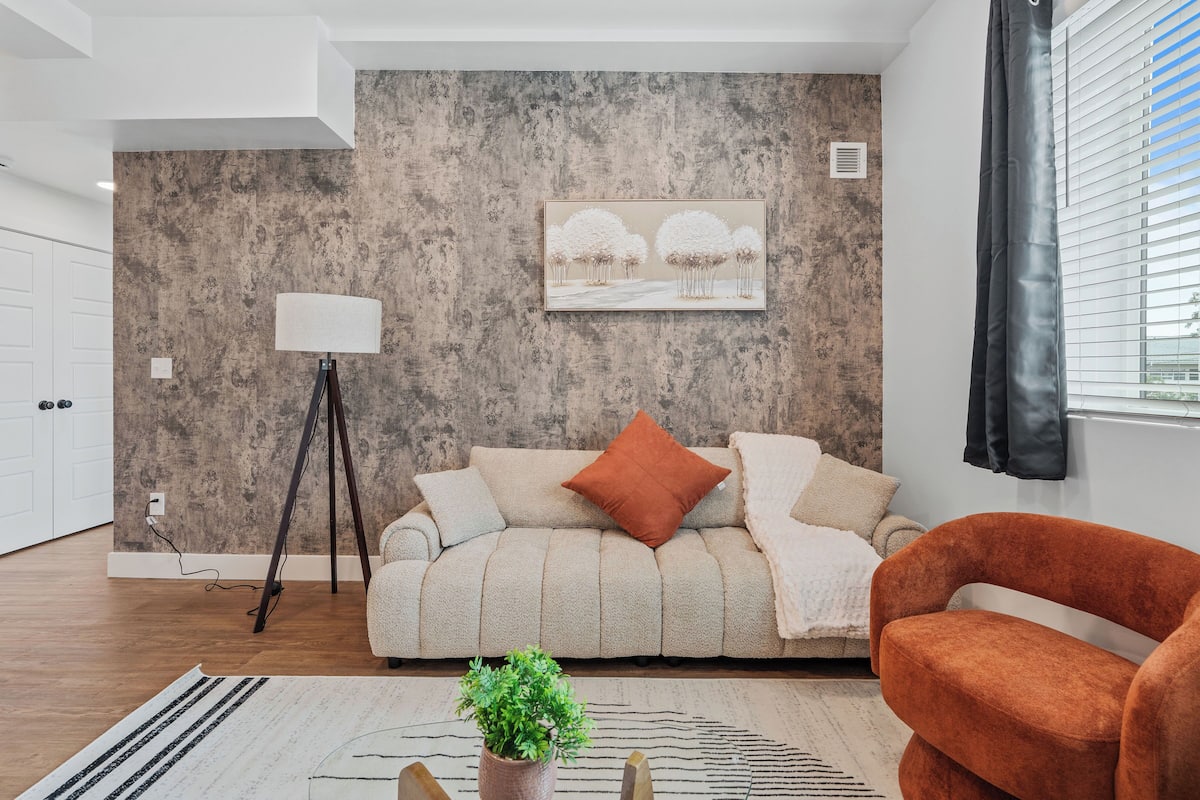 Un salon moderne avec un canapé, une lampe sur pied, une plante en pot et une fenêtre avec des stores.