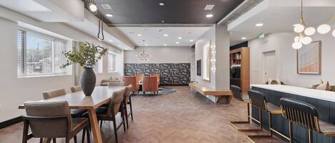 A modern interior with a herringbone wooden floor, a central dining table, bar seating, and a chandelier.