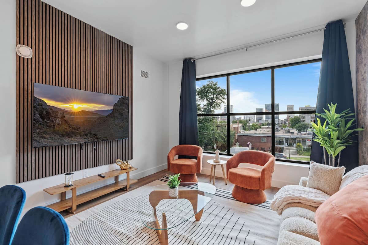 Un salon moderne doté d’un grand téléviseur, de sièges confortables, d’une table basse et offrant une vue sur la ville.