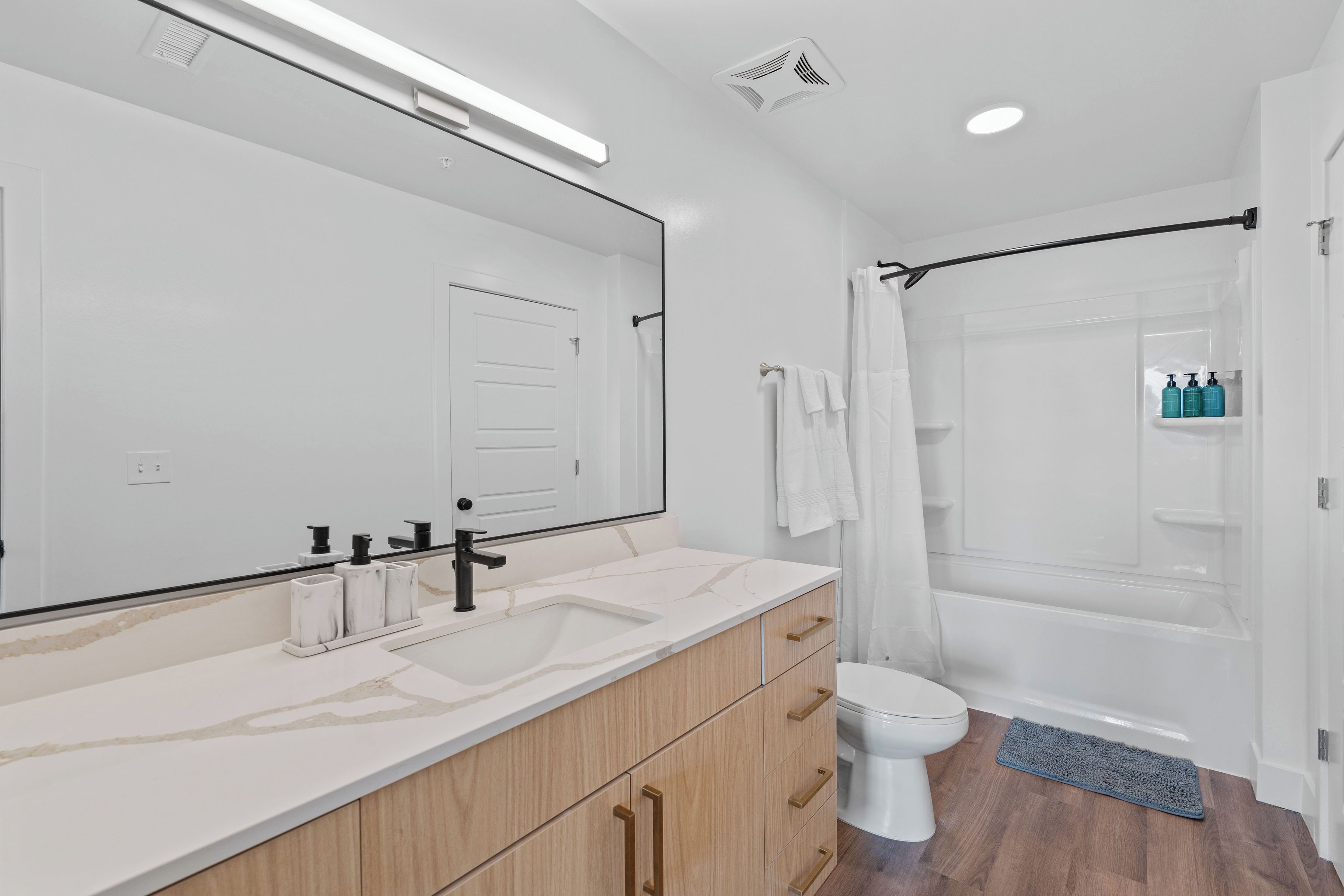 A modern bathroom with a large mirror, a sink, a toilet, and a shower area.