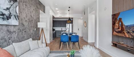 A modern living room with a sofa, a coffee table, and a dining area with blue chairs.