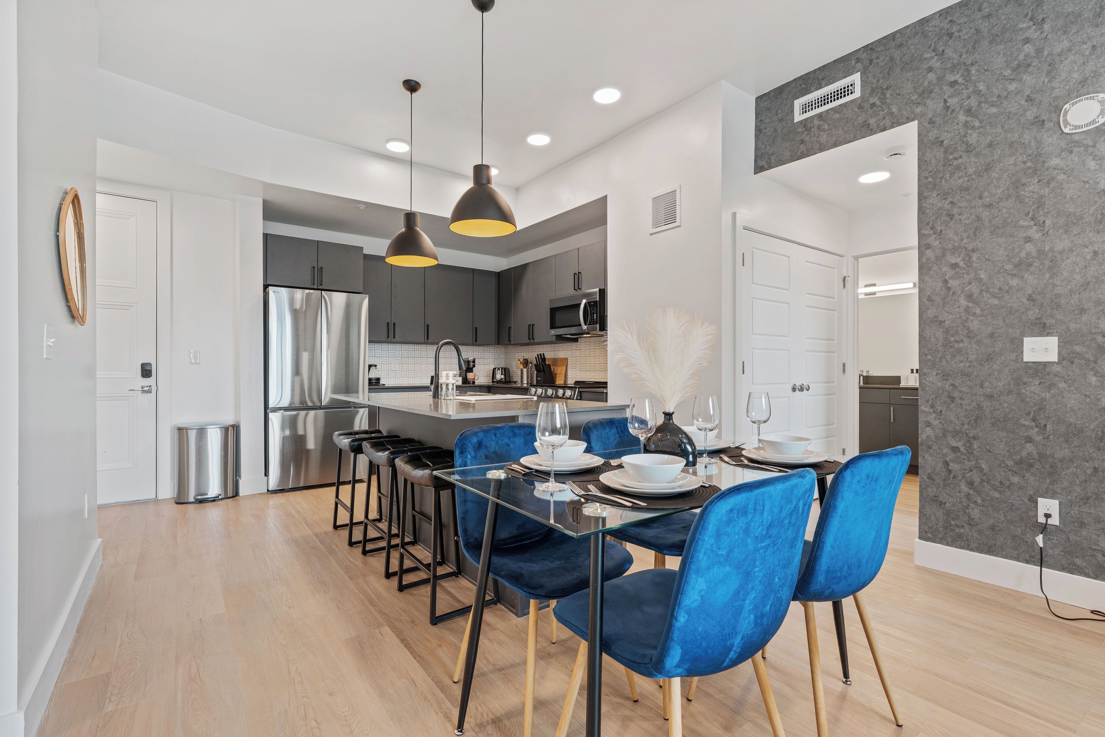 Una cocina moderna con electrodomésticos de acero inoxidable, un comedor con sillas azules y una pared gris con textura.