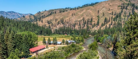 A river flowing through a valley with a building with a red roof and a small cabin nearby.