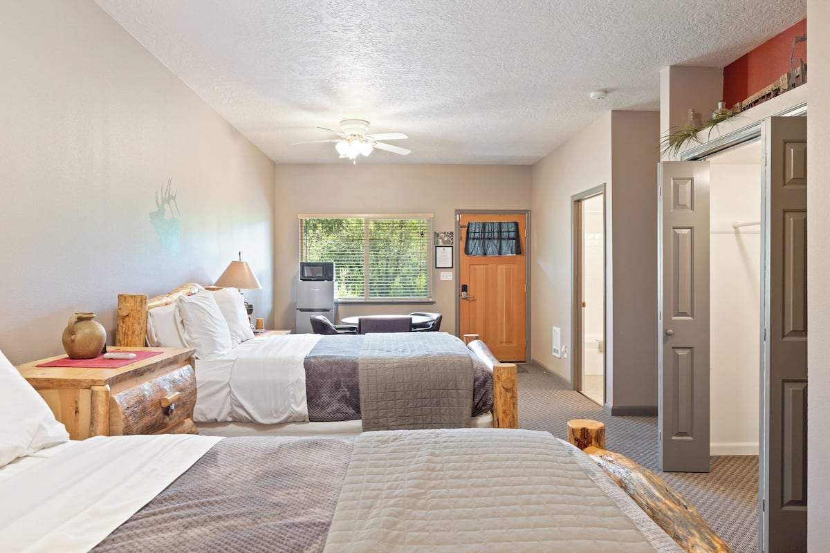 A hotel room with two beds, a desk, a chair, a television, and a door.