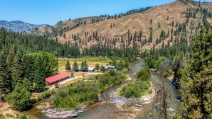 A river flowing through a valley with a building with a red roof and a small cabin nearby. - SouthFork Lodge (Lowman)
