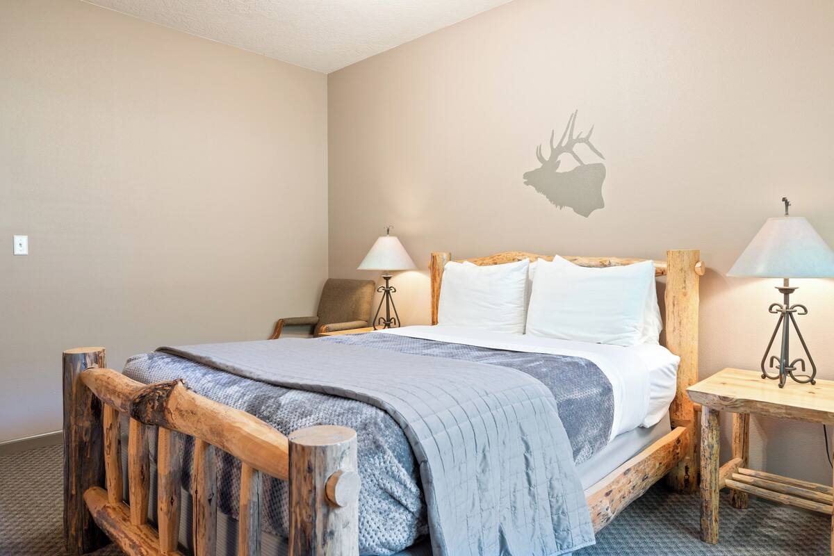 A bed with a wooden headboard, a wall-mounted deer silhouette, and two bedside lamps.