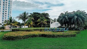 A landscaped area with a sign reading 'PLAYA BLANCA,' palm trees, and a modern building in the background. - Blue Escape Suite (rio hato)