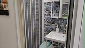 A bathroom with a striped shower curtain, a sink with a mirror, and a patterned wall. - One-room/studio apartment in Sperlonga. (Sperlonga)
