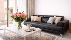 Una sala moderna con un sofá de cuero negro, una mesa de centro blanca y un jarrón con flores rosas.