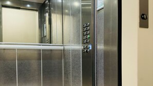 Un ascensor con panel de control, paredes metálicas y suelo de baldosas.